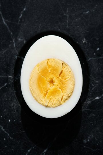Macro overhead of a halved hard boiled egg showing fully set pale golden yolk, no gray ring, on black marble