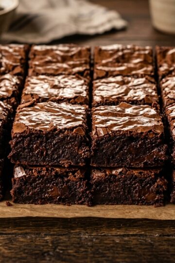 Double fudge brownies with crackly top and fudgy interior cut into 16 squares on dark wood surface